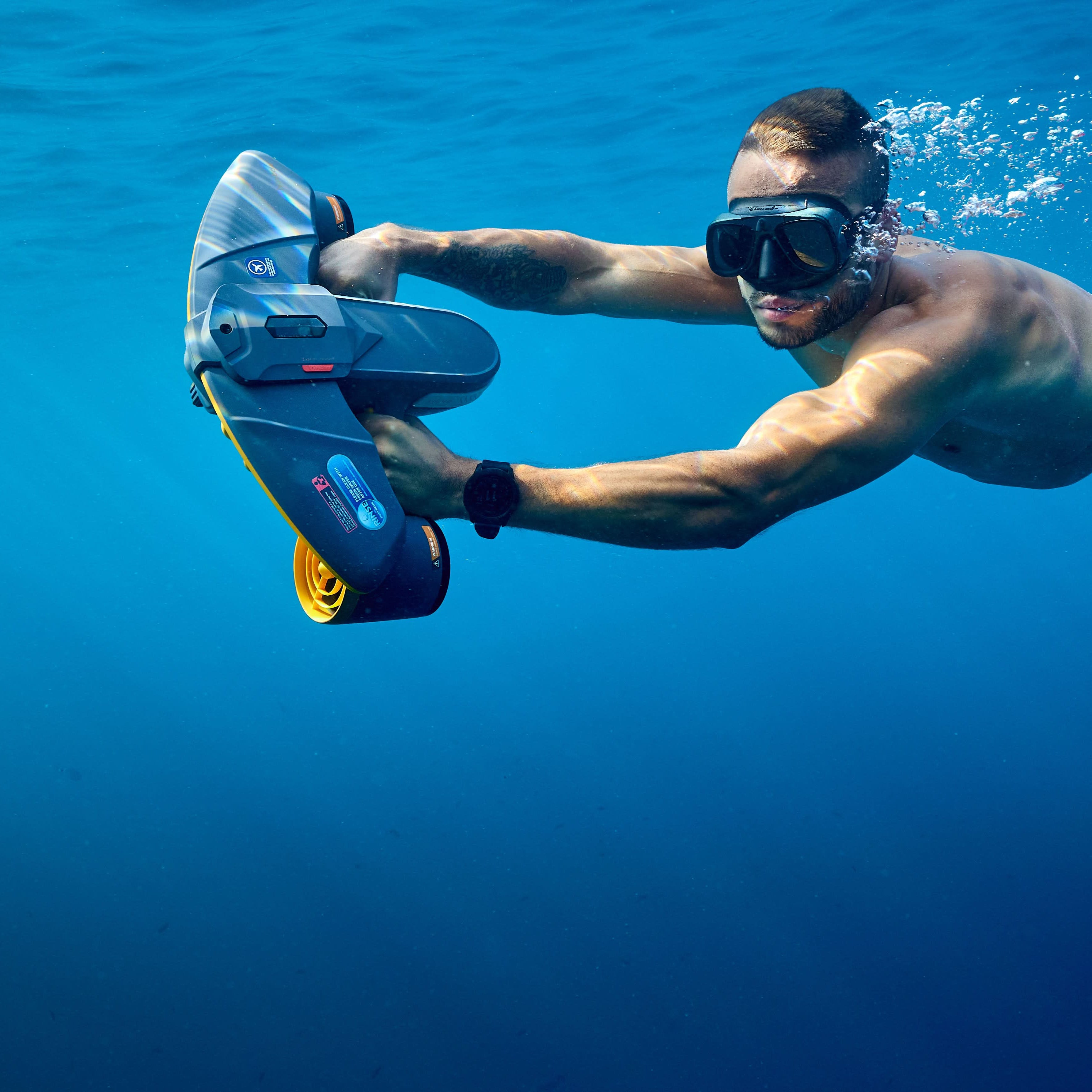 Diver in red shorts using SUBLUE Navbow+ underwater scooter in clear blue water.