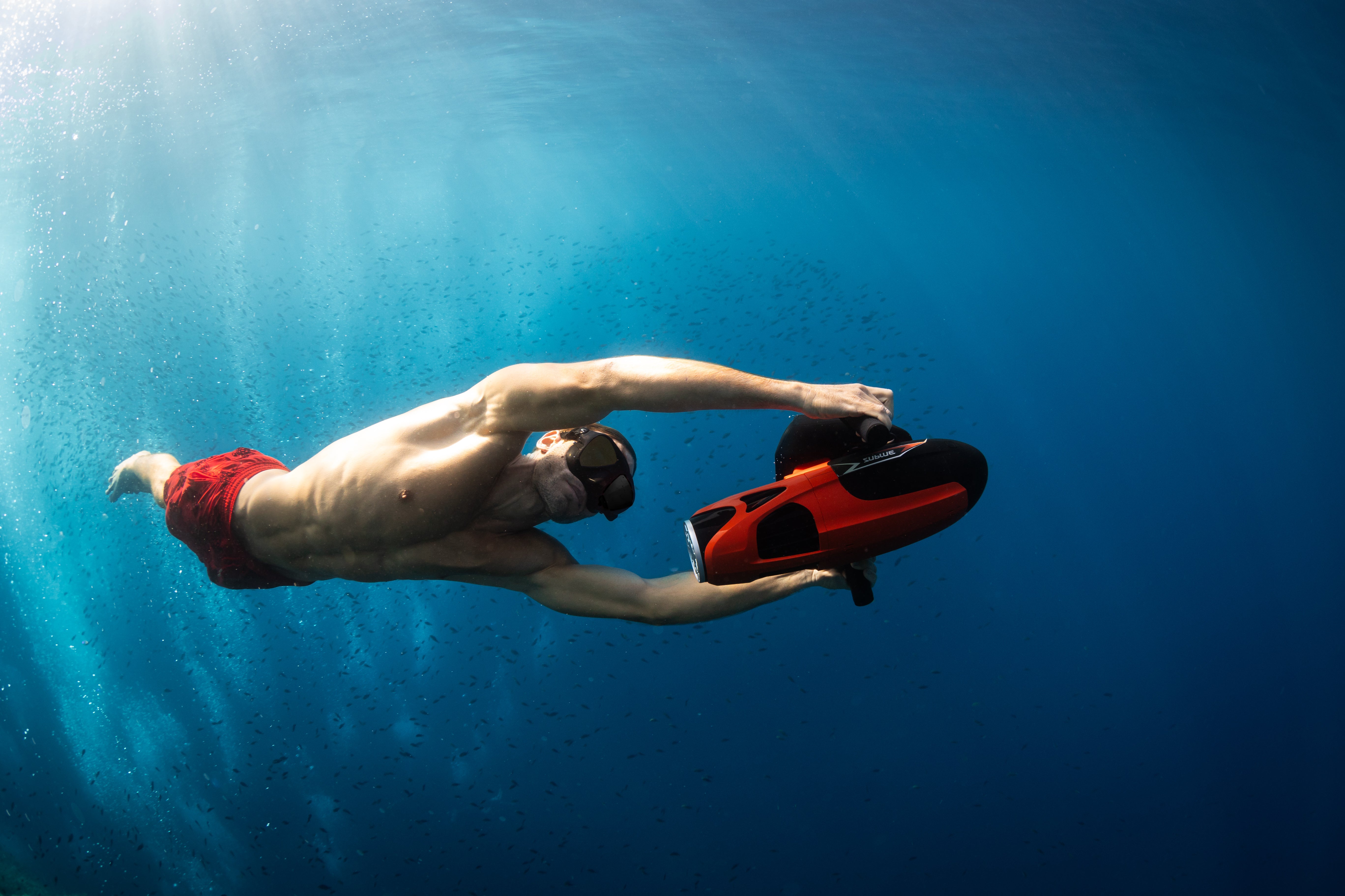 A man is swimming underwater with an underwater scooter, exploring the ocean floor.