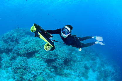 Diver exploring underwater with Sublue scooter in coral reef.