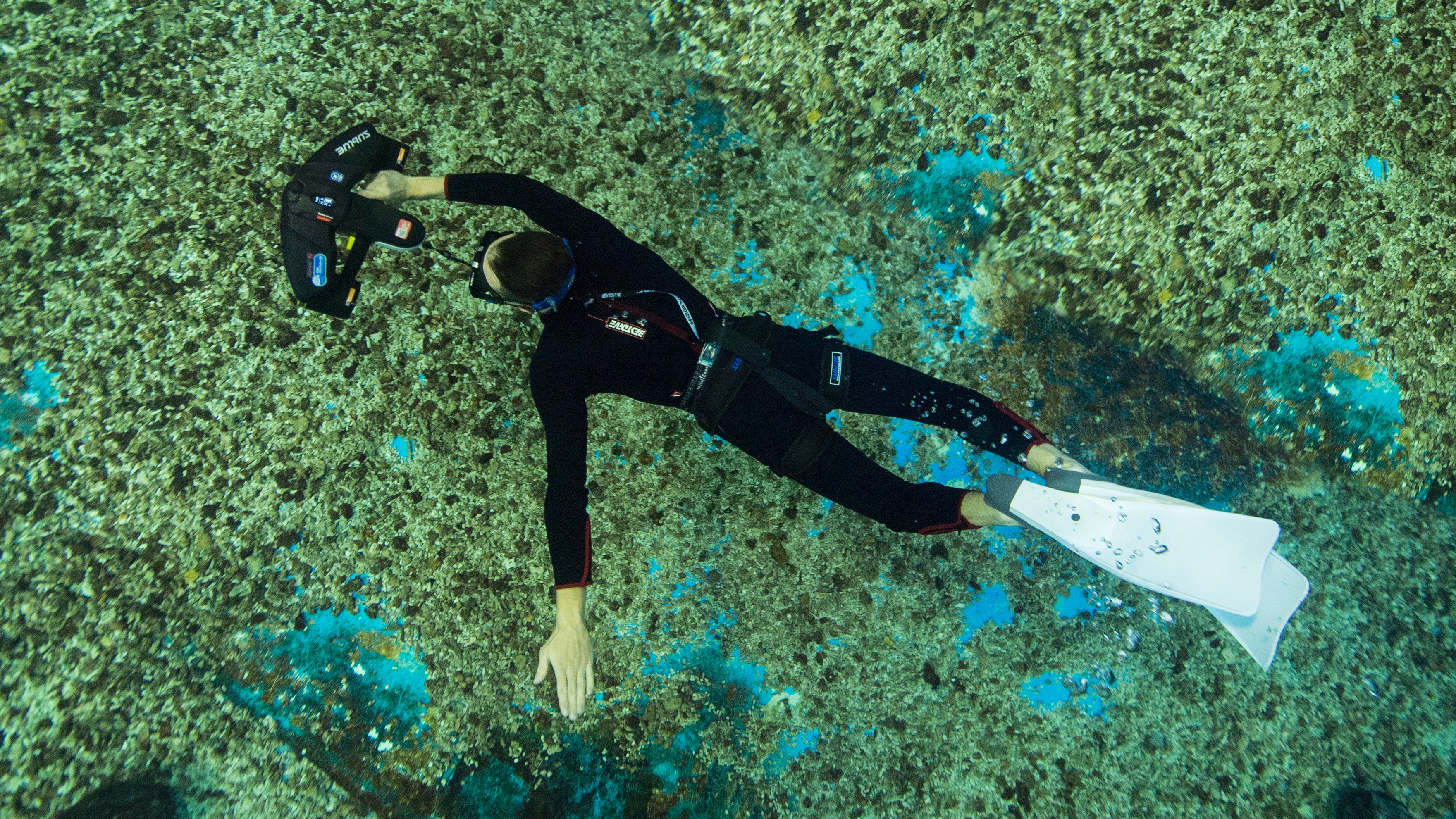 Diver swimming with Sublue scooter and Diving Cross Strap in a coral reef.