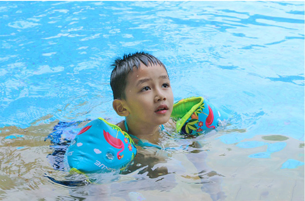 Boy floating in blue pool with parrot design inflatable swim armbands.