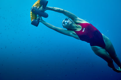 Diver in red swimsuit using SUBLUE Navbow+ scooter underwater in clear blue water.