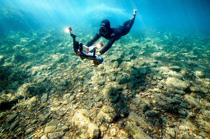 Diver using Sublue waterproof LED light while exploring rocky underwater terrain.