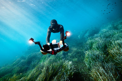 Diver in black wetsuit operating Sublue LED lights with underwater camera in seagrass.