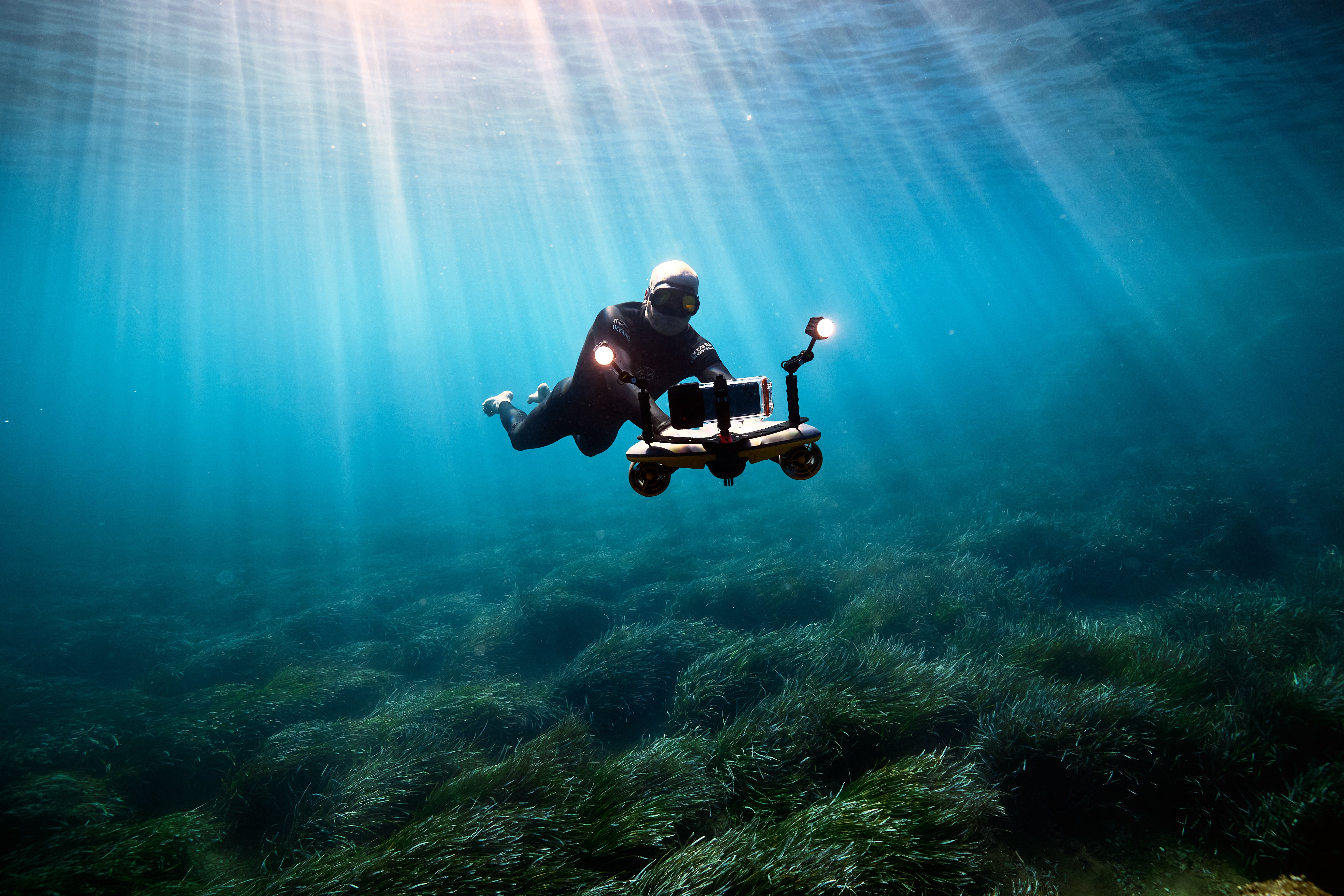 Diver on Sublue scooter with LED lights exploring seagrass underwater.