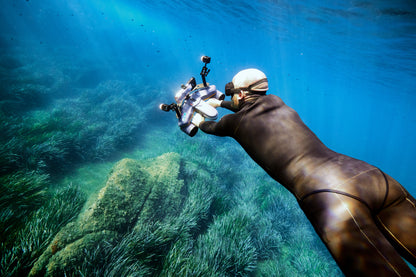 Diver in black wetsuit using underwater camera rig in clear waters.