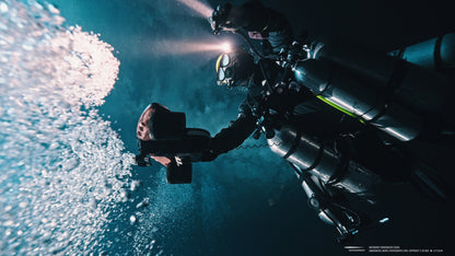 Diver operating Sublue Waterproof LED Light in deep water with bubbles.