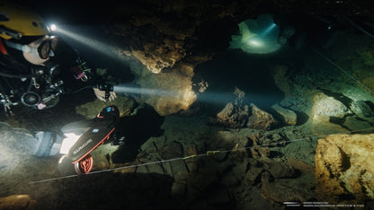 Diver using Sublue scooter and LED lights exploring underwater cave with rocky terrain.