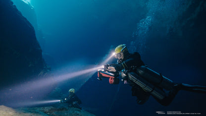 Divers using SUBLUE Navbow scooters in underwater cave with bright headlights.