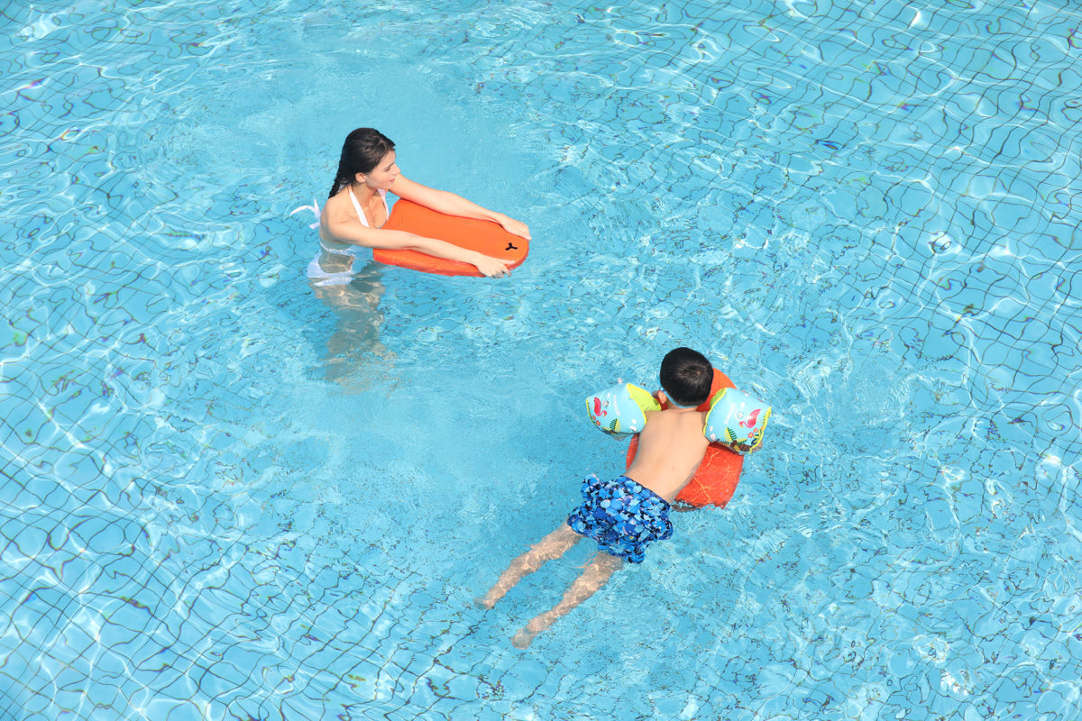 Adult holding swim board while child floats with colorful inflatable armbands in pool.