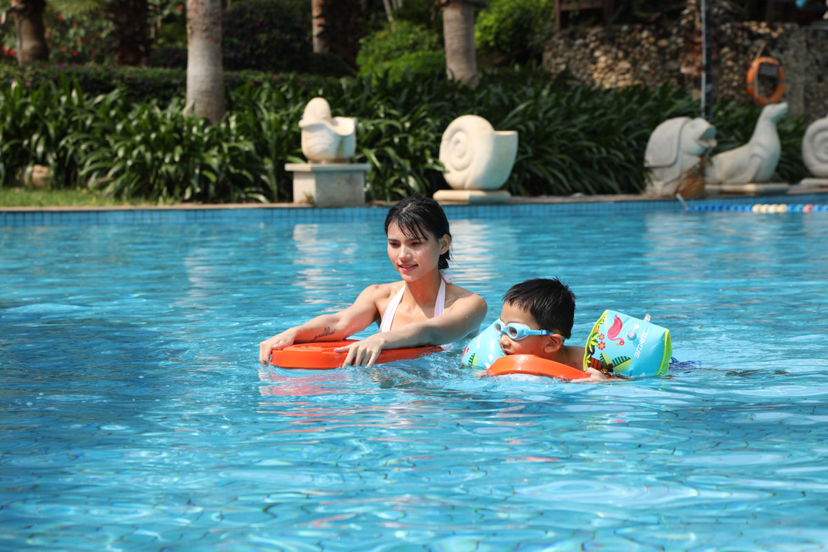 Adult assisting child with inflatable armbands in a sunny blue pool