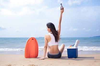 Woman holding SUBLUE Swii kickboard, sitting on the beach by the water.