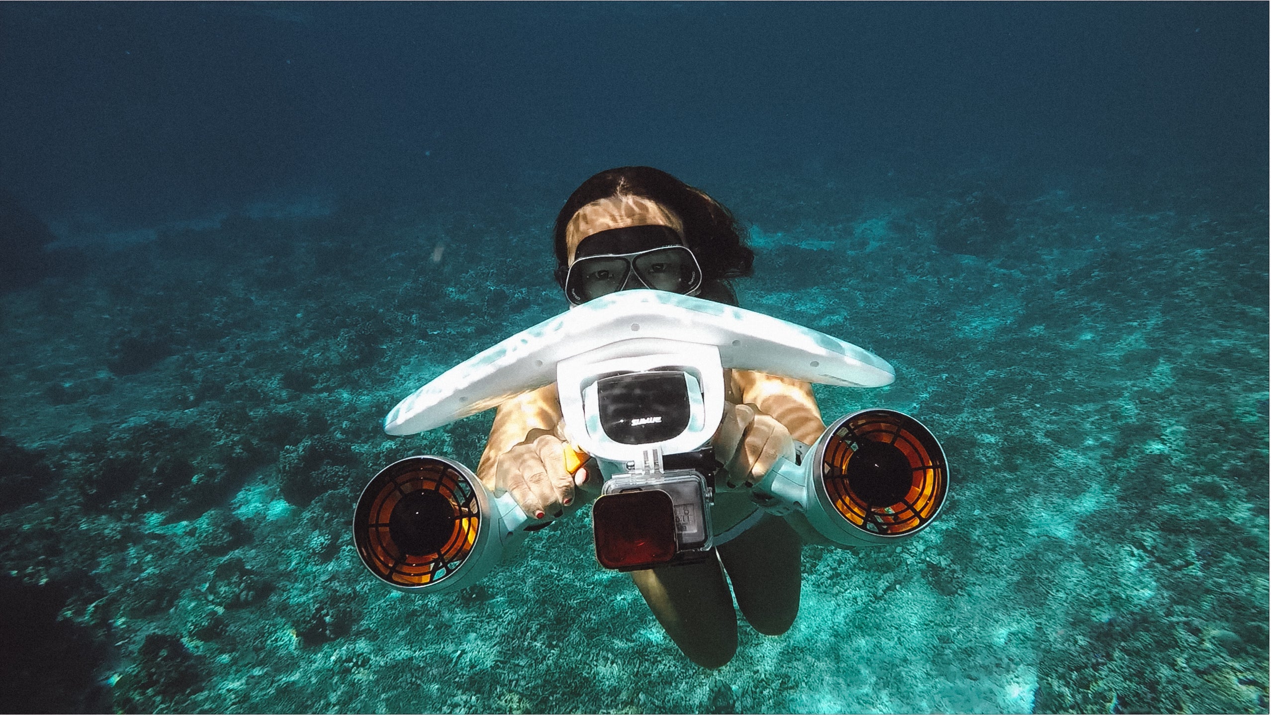 Diver using Sublue Mix underwater scooter with orange propellers in clear blue water.