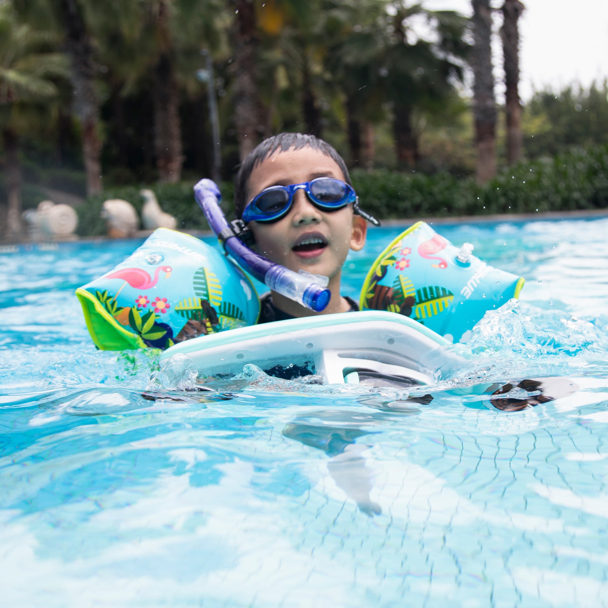 Child with snorkel and goggles, wearing bright inflatable swim armbands in pool.