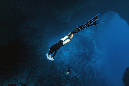 Diver using Sublue underwater scooter with fins in deep ocean water.