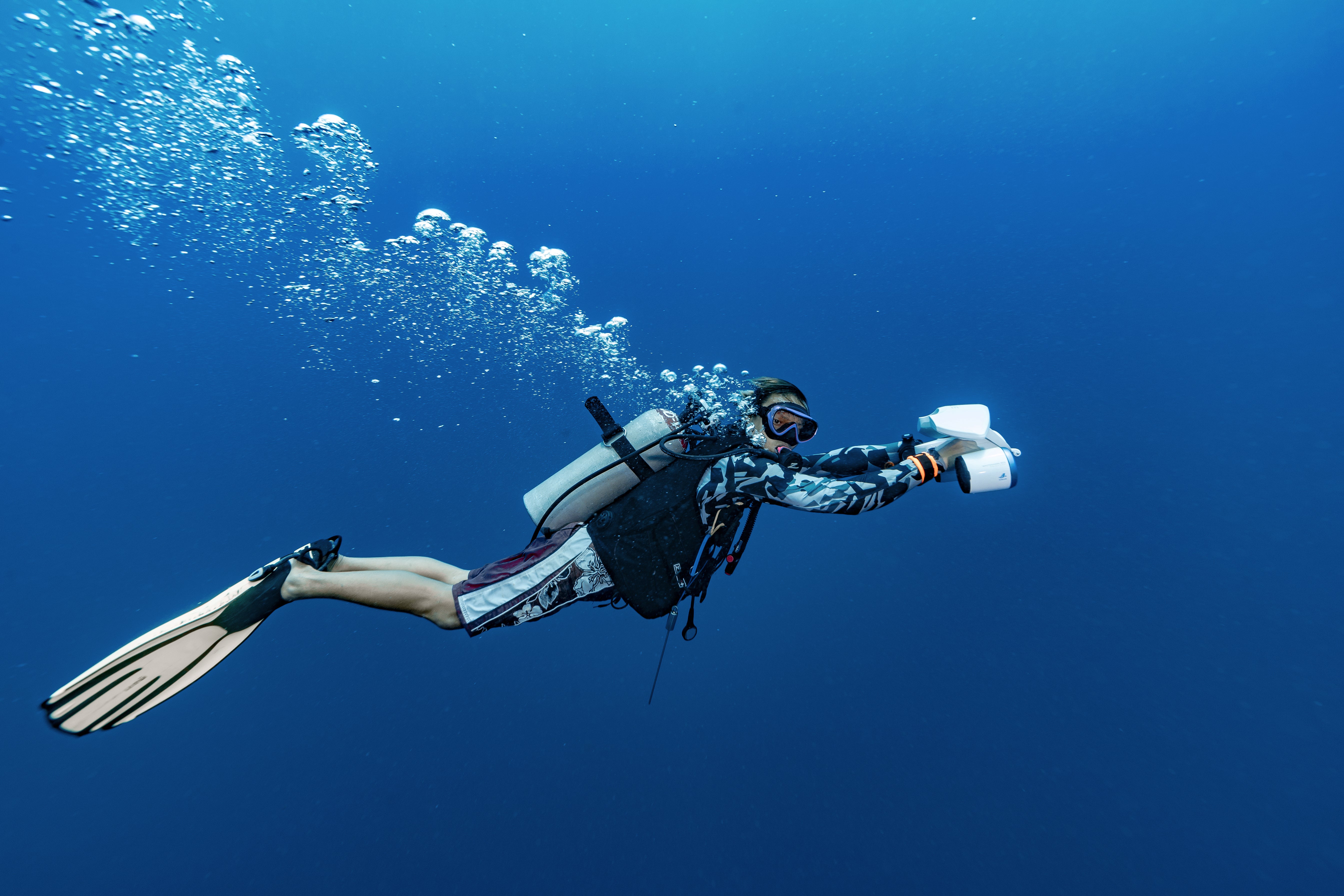 Diver using Sublue underwater scooter in blue waters with fins and bubbles.