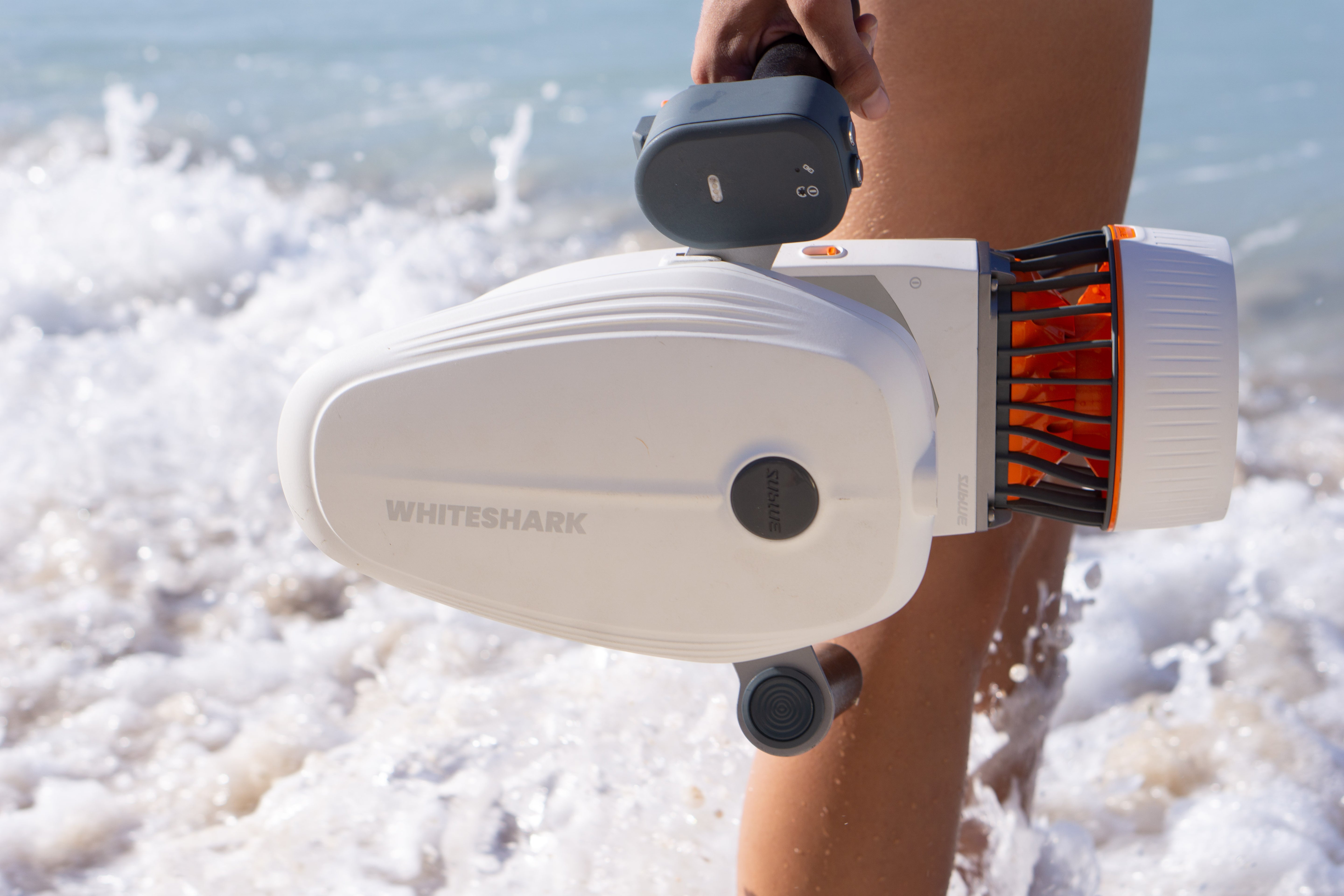 Person holding Whiteshark underwater scooter at the beach, ready for exploration.