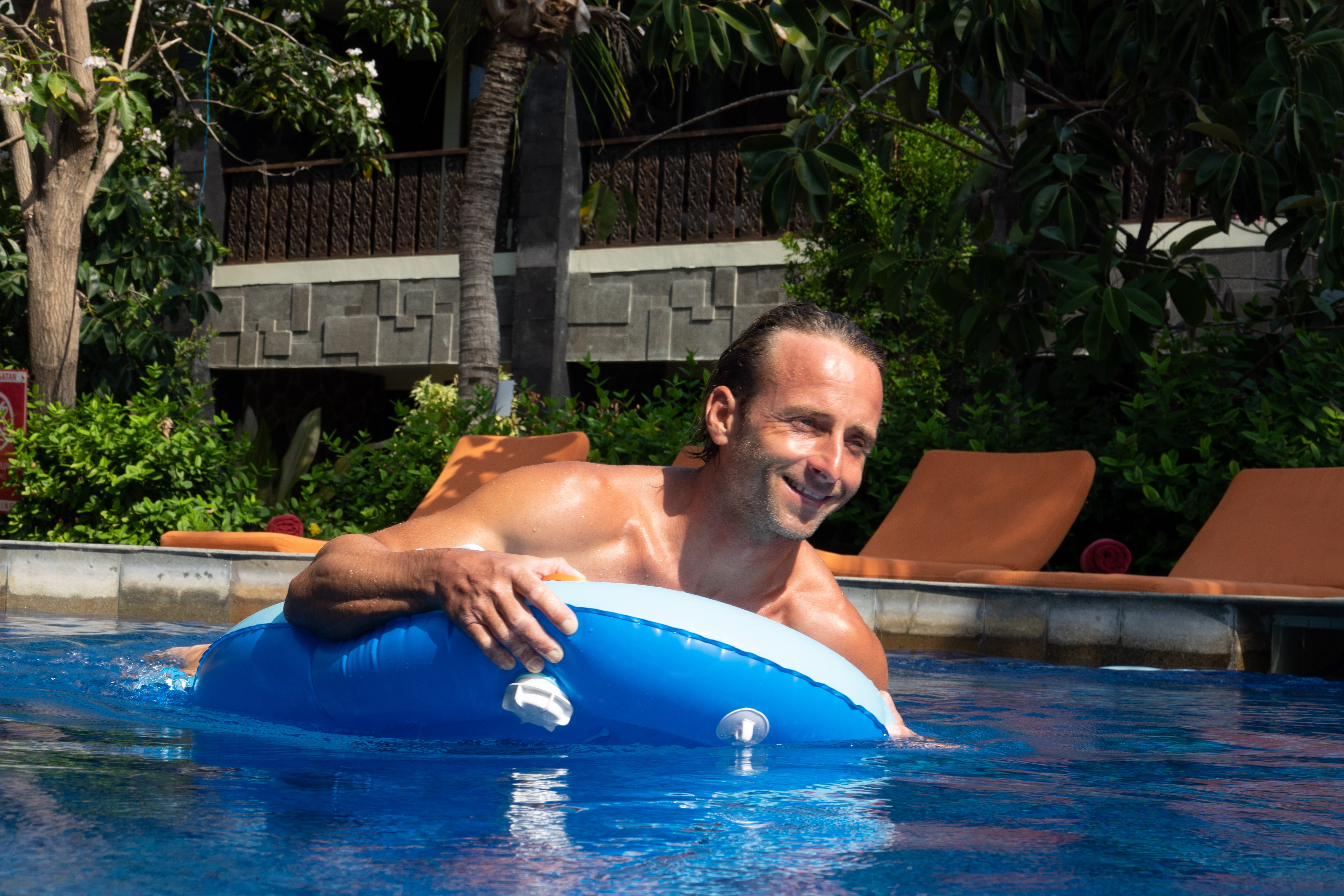 Man relaxing on blue inflatable kickboard in sunny pool.