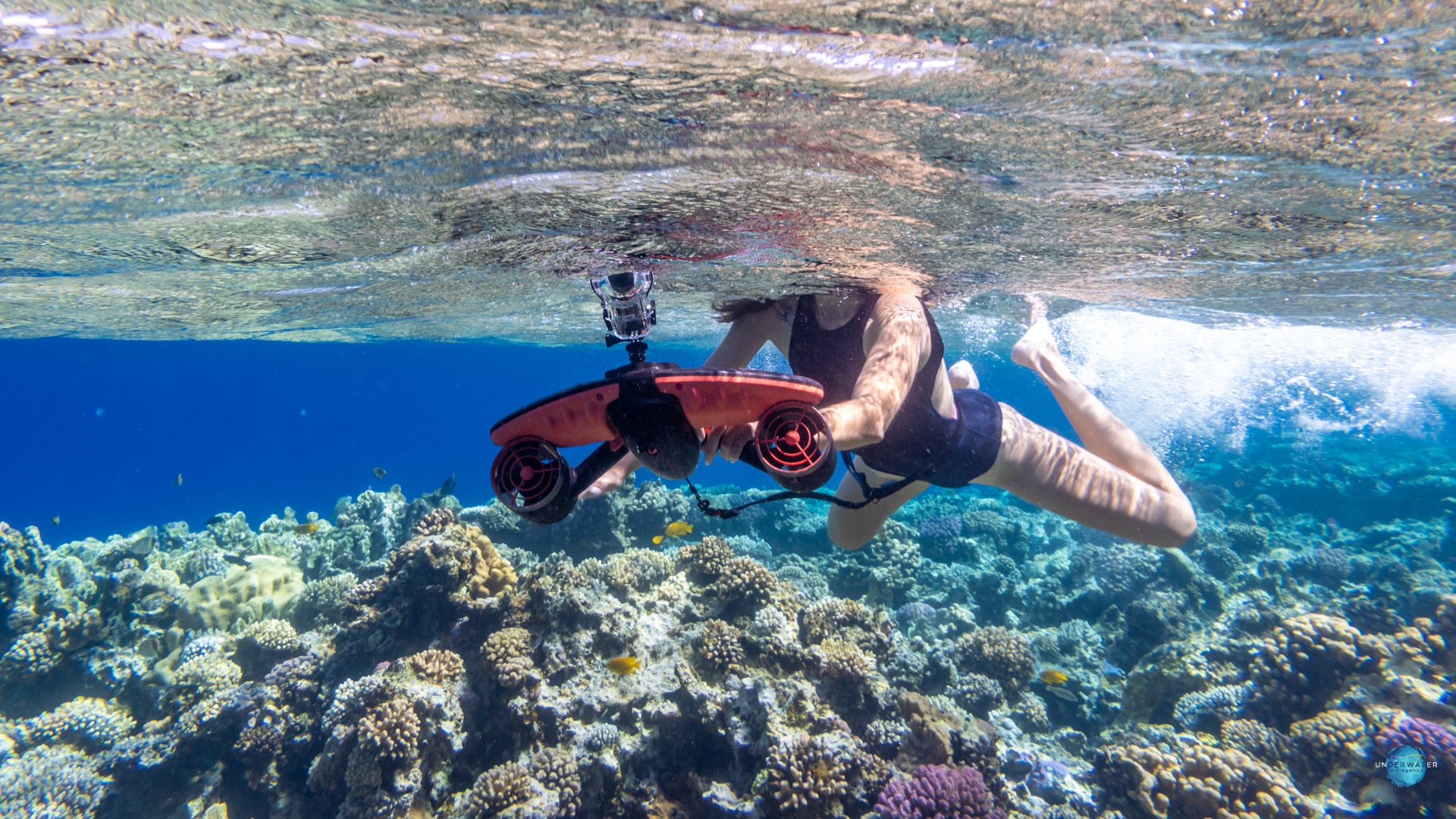 Diver using Sublue underwater scooter exploring colorful coral reef.