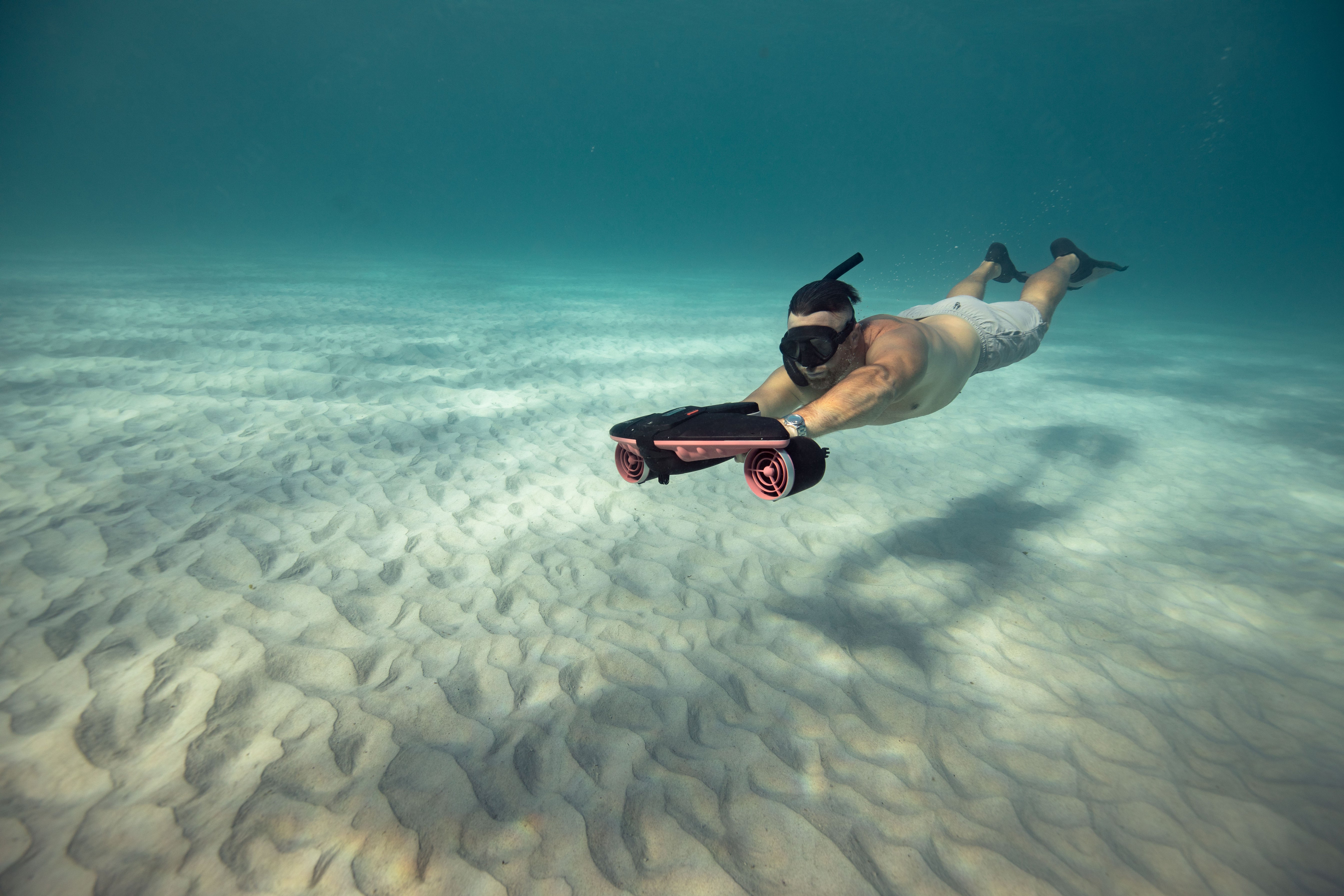 Diver gliding underwater with SUBLUE Navbow scooter over sandy seabed.