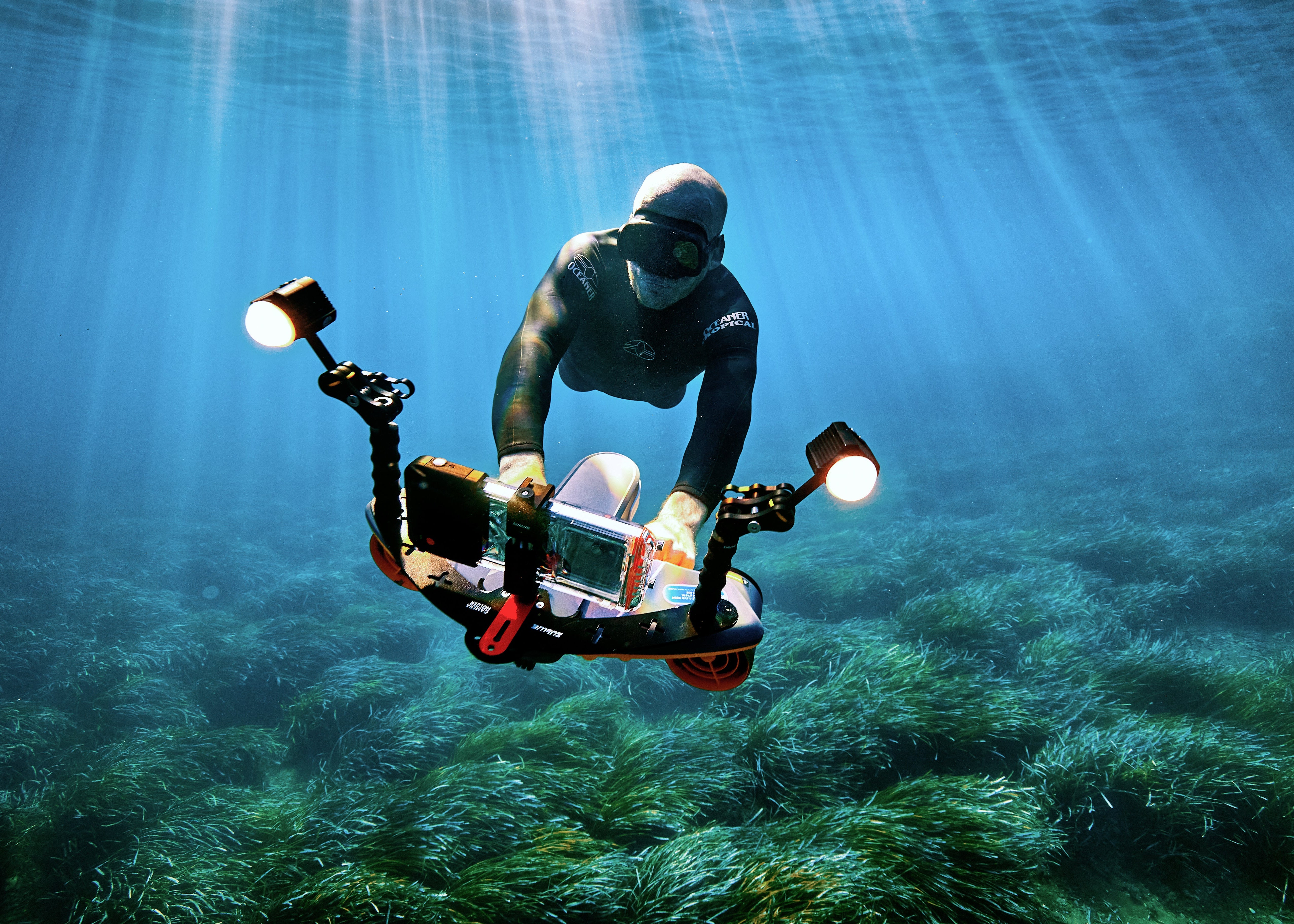 Diver using Sublue underwater scooter with smartphone mount and lights in clear waters.