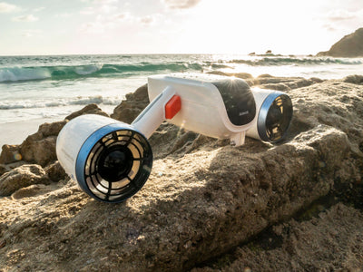 Sublue Mix underwater scooter on rocky beach during sunset.