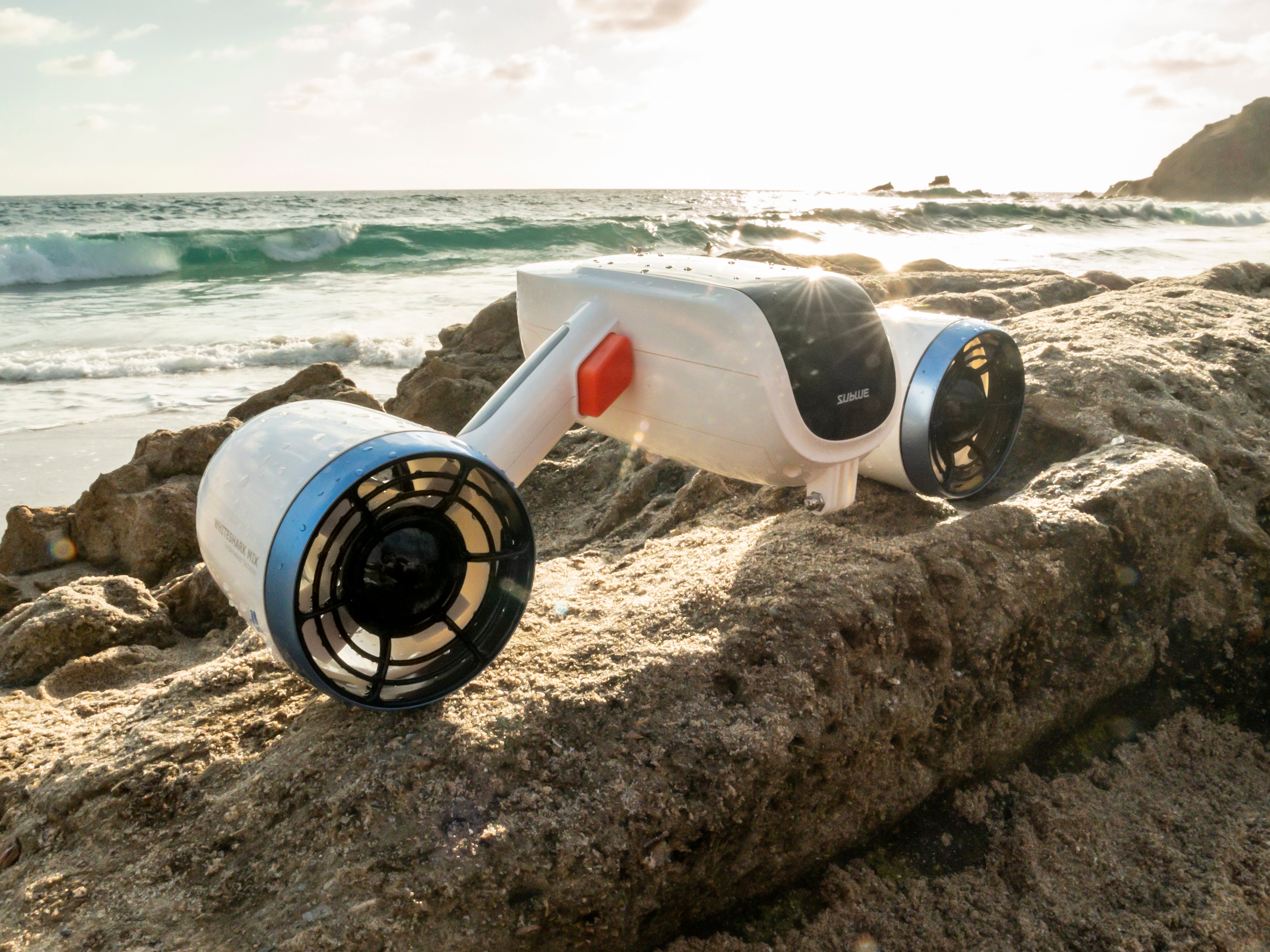 Sublue Mix underwater scooter on rocky beach during sunset.