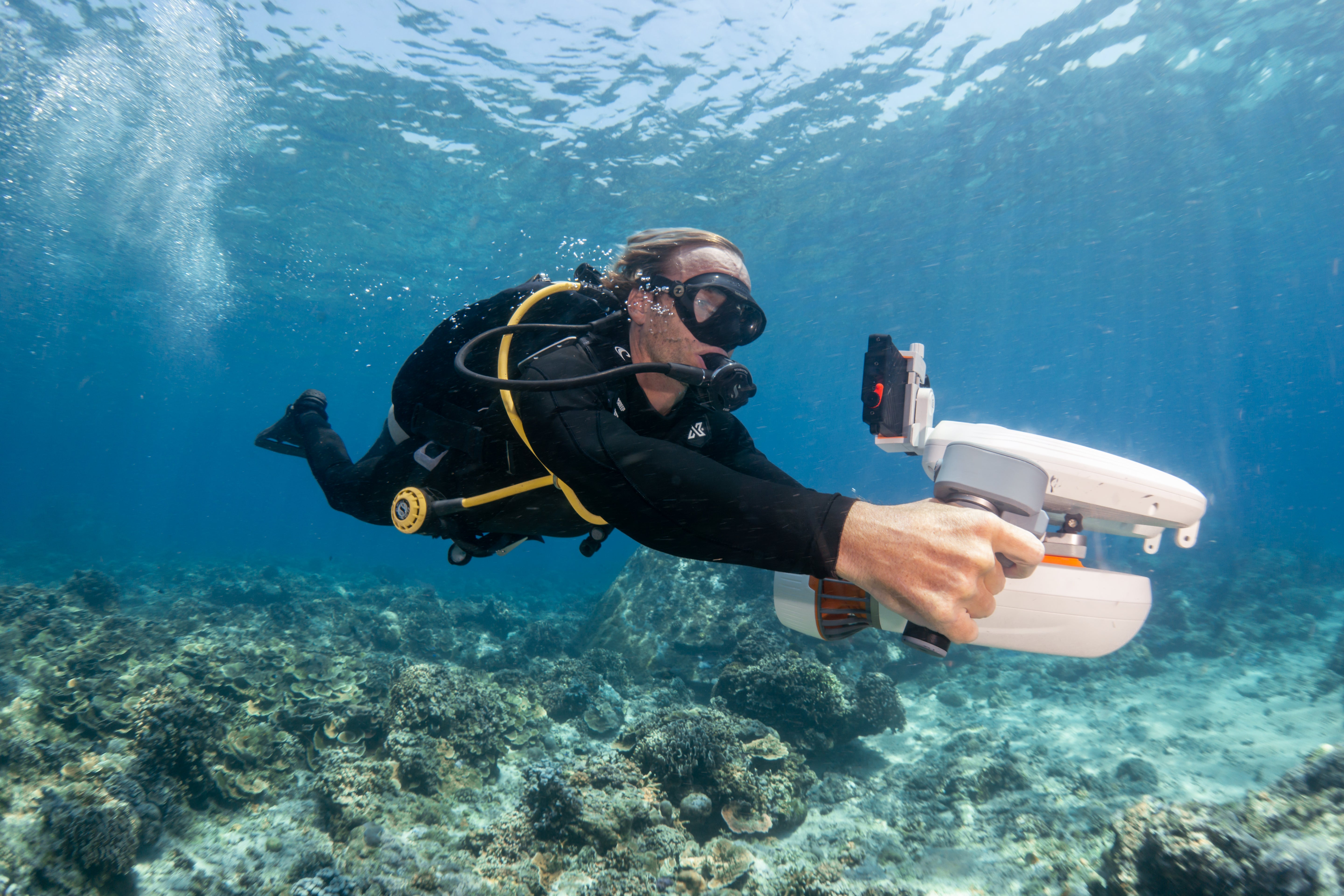 Diver with Tini Floater on underwater scooter exploring a coral reef.