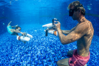 Diver capturing photo of person using underwater scooter in pool