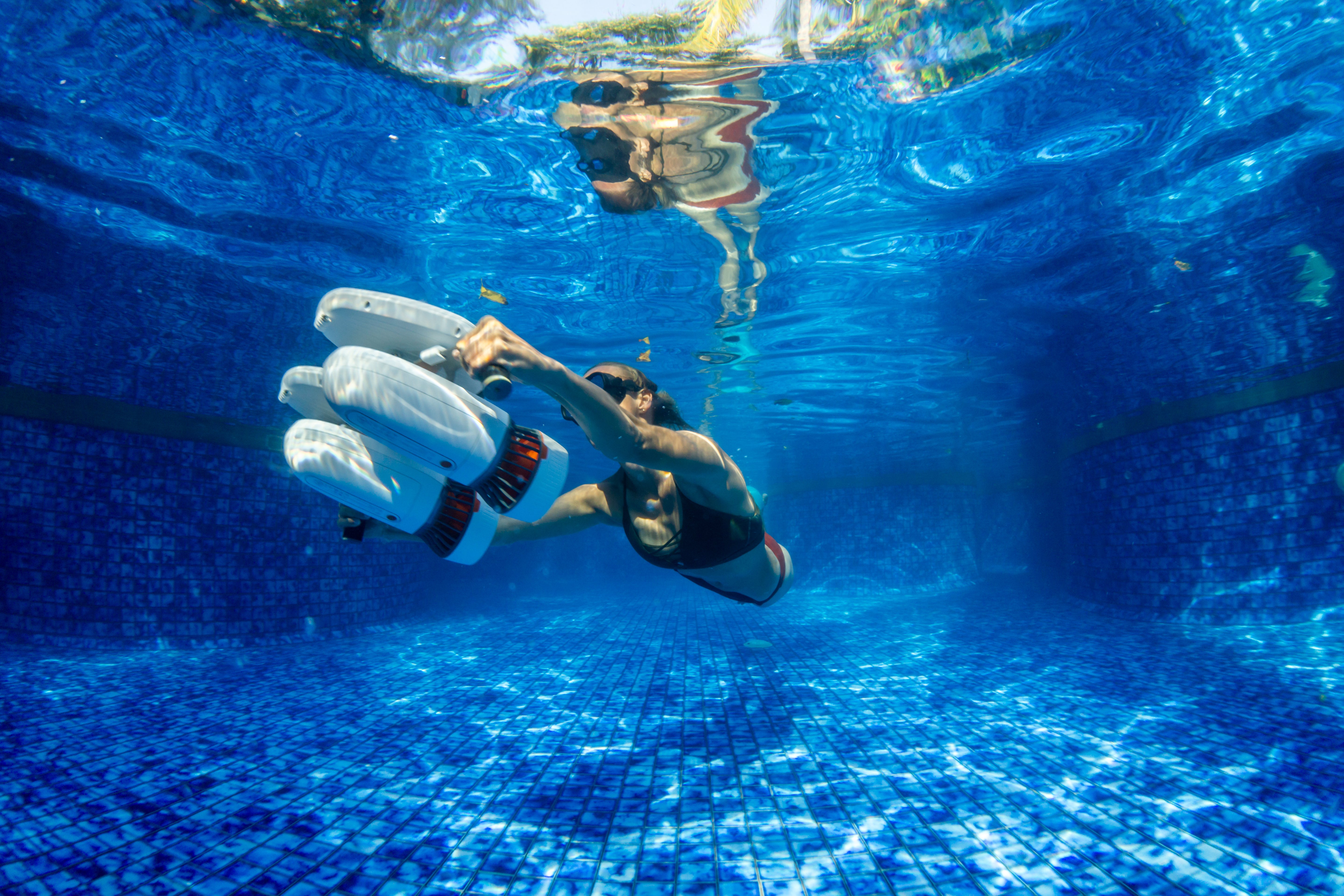 Diver holding Tini Floater with underwater scooter, swimming in a clear pool.