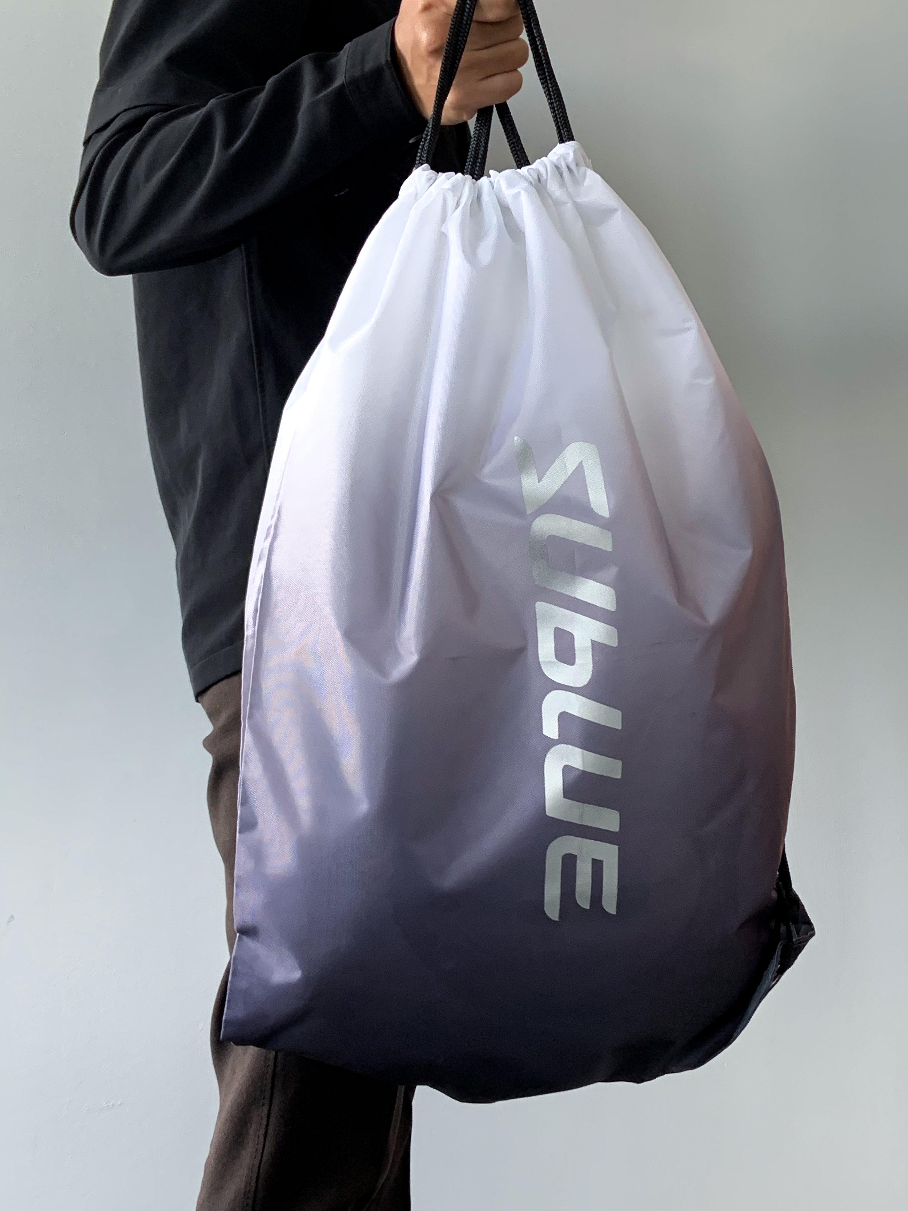 Person holding Sublue drawstring backpack with gray-to-white gradient.