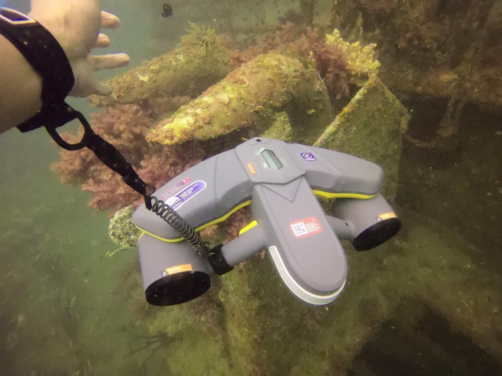 Diver's hand near a coral structure with Sublue underwater scooter and anti-lost lanyard.